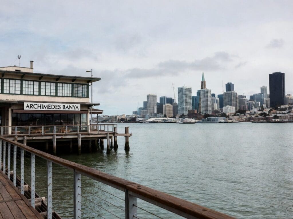 a photograph of the San Francisco Bay waterfront near Archimedes Banya, emphasizing the deck, skyline, and calm water rather than guests