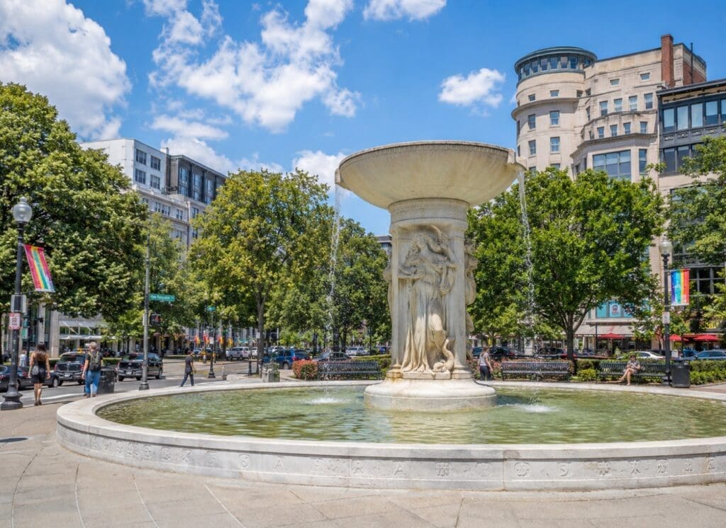 an original photo of Dupont Circle fountain with nearby rainbow flags and neighborhood streets