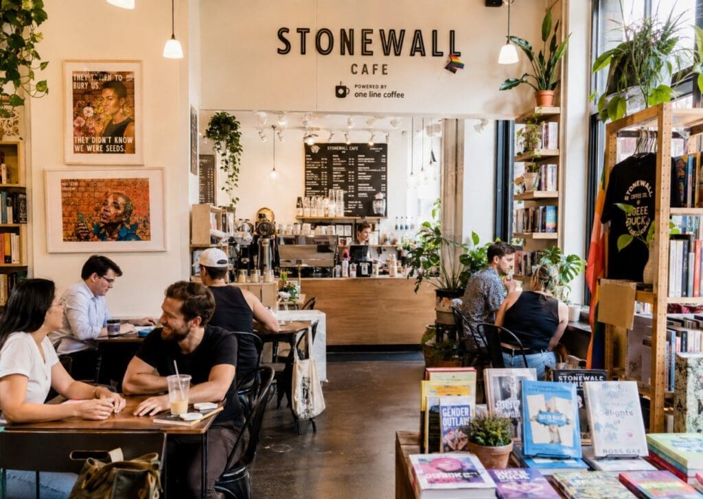 original photo of Stonewall Cafe showing books, local art, plants, and visitors socializing