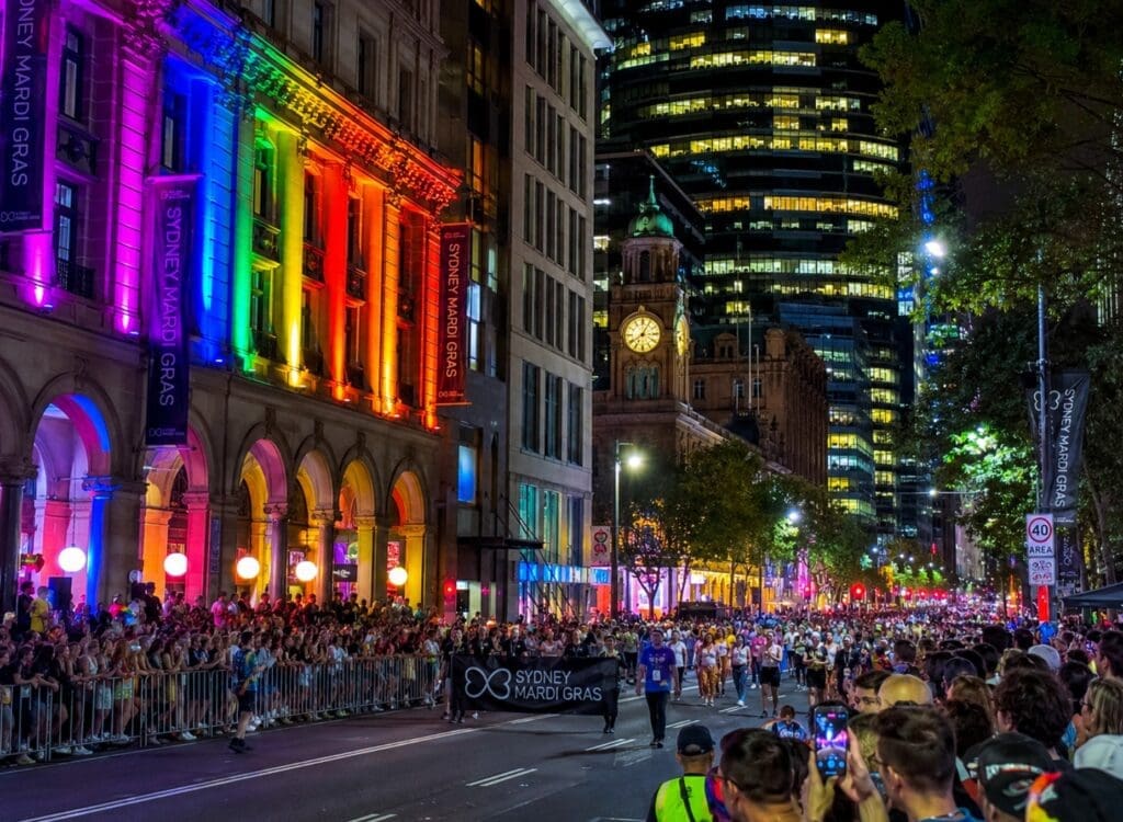 photograph of Sydney’s Oxford Street during Mardi Gras, showing rainbow lighting, spectators, and city architecture
