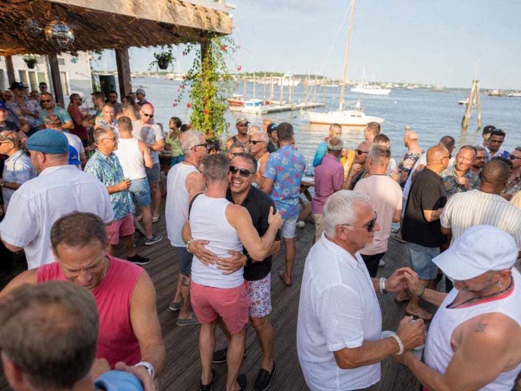 photograph of the Boatslip deck during Tea Dance, showing the harbor, colorful clothing, and an inclusive afternoon crowd