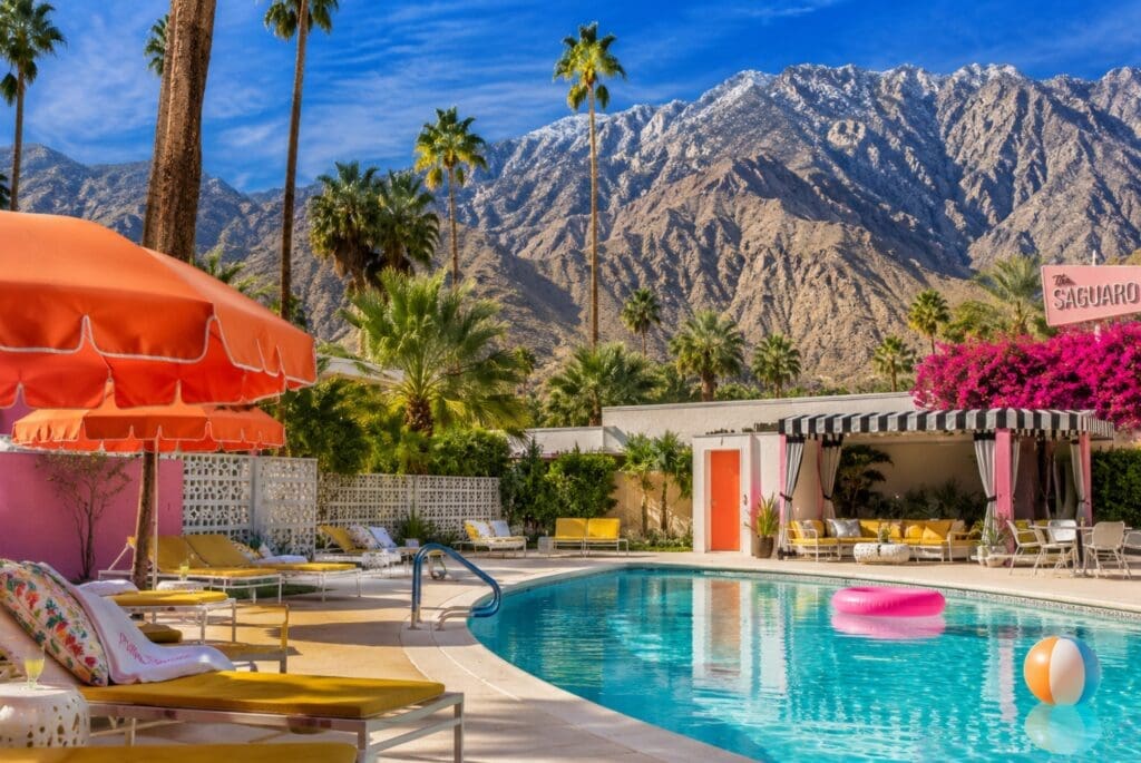photograph of the San Jacinto Mountains towering above a midcentury-modern Palm Springs pool, with palm trees and shaded loungers in the foreground