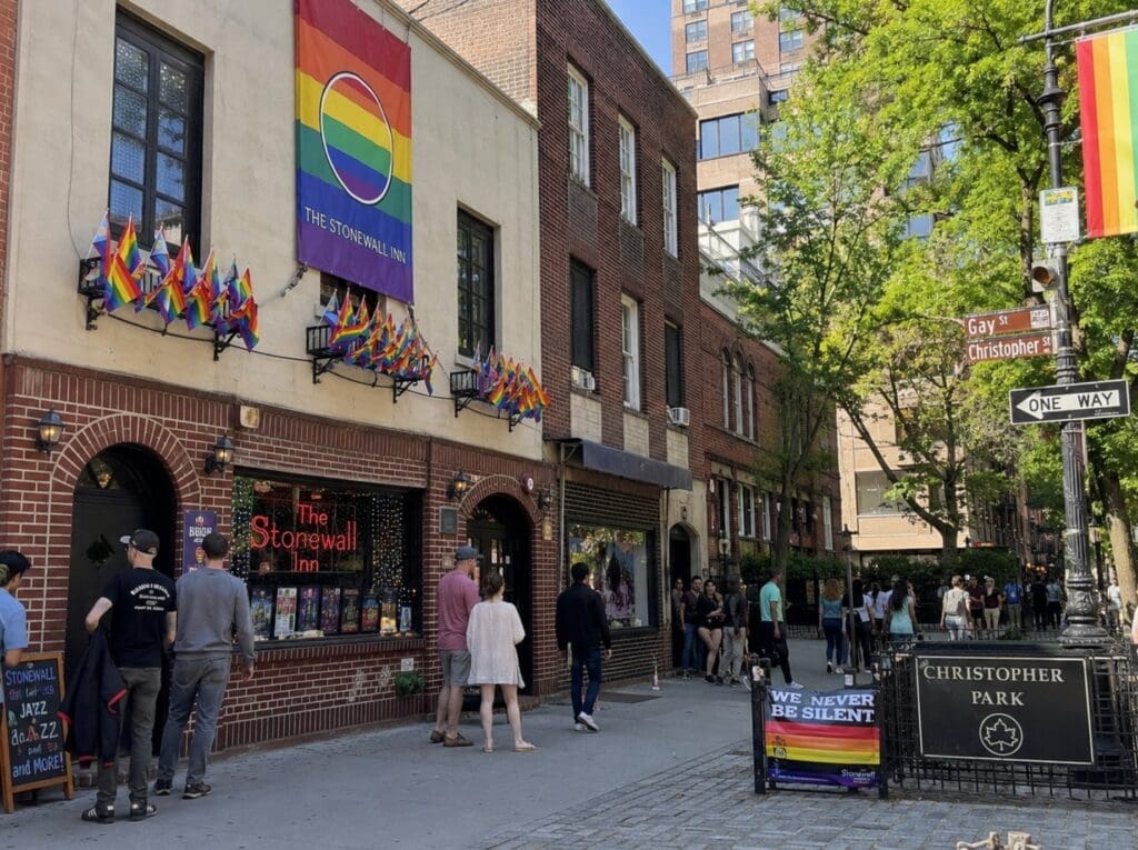 photograph of the Stonewall Inn and Christopher Park in New York City, with pedestrians and rainbow flags