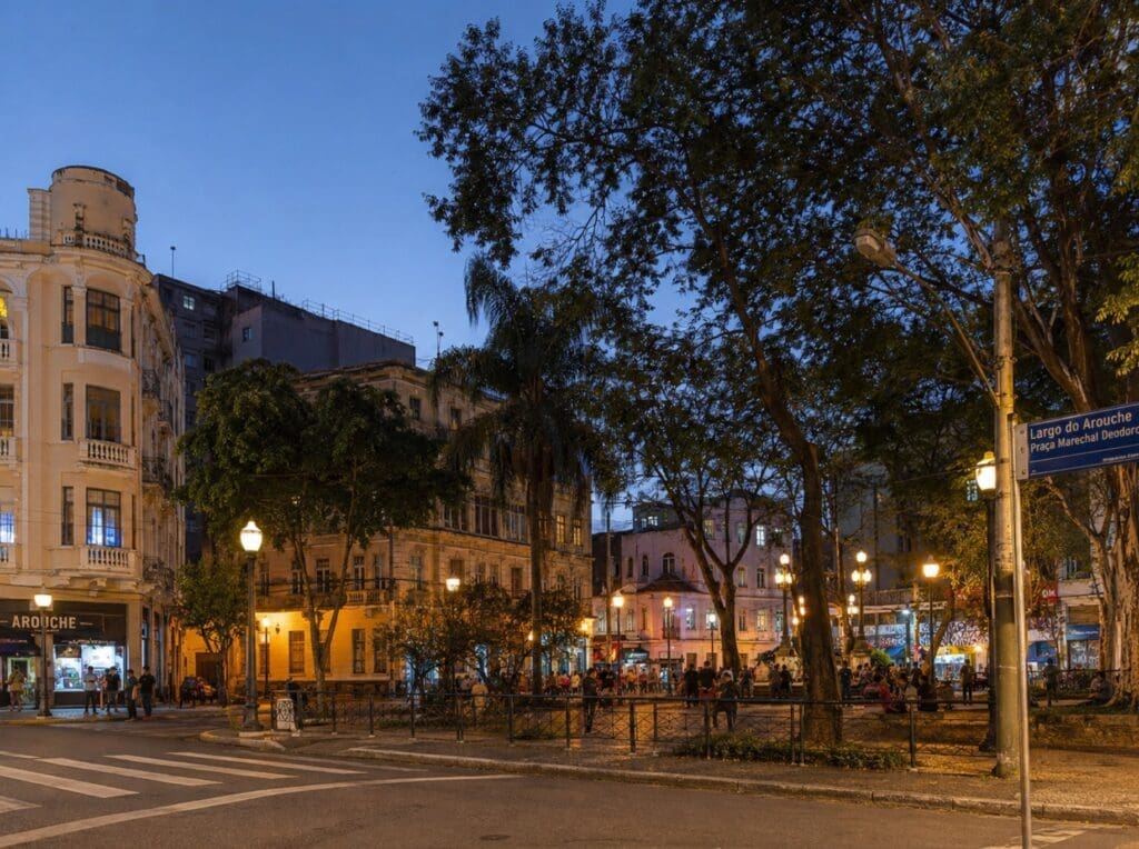 uma fotografia do Largo do Arouche ao entardecer, com árvores, prédios antigos e movimento urbano