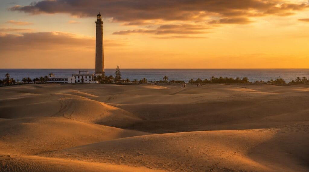 una fotografía  de las dunas de Maspalomas al atardecer, con el faro y el océano al fondo