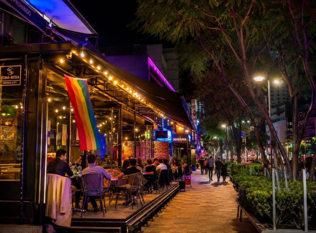 una fotografía de una terraza de Zona Rosa al comienzo de la noche, con grupos conversando y luces de colores (mexico city)
